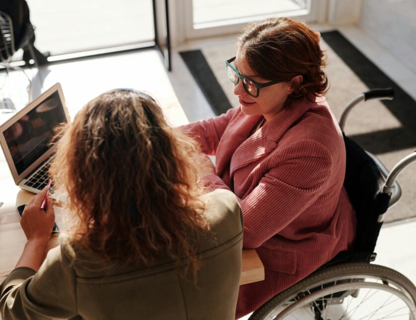 Woman in wheelchair and carer sat at desk with laptop